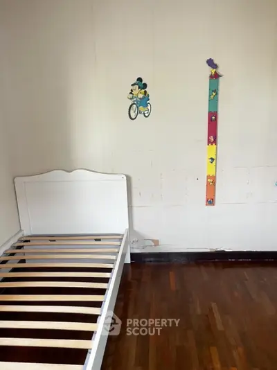 Spacious bedroom with wooden flooring and playful wall decor, perfect for a child's room.