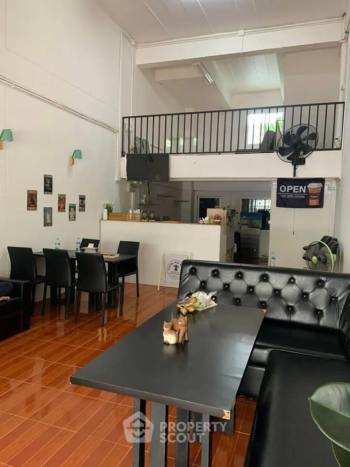 Spacious modern living area with mezzanine, sleek black furniture, and warm wooden flooring.