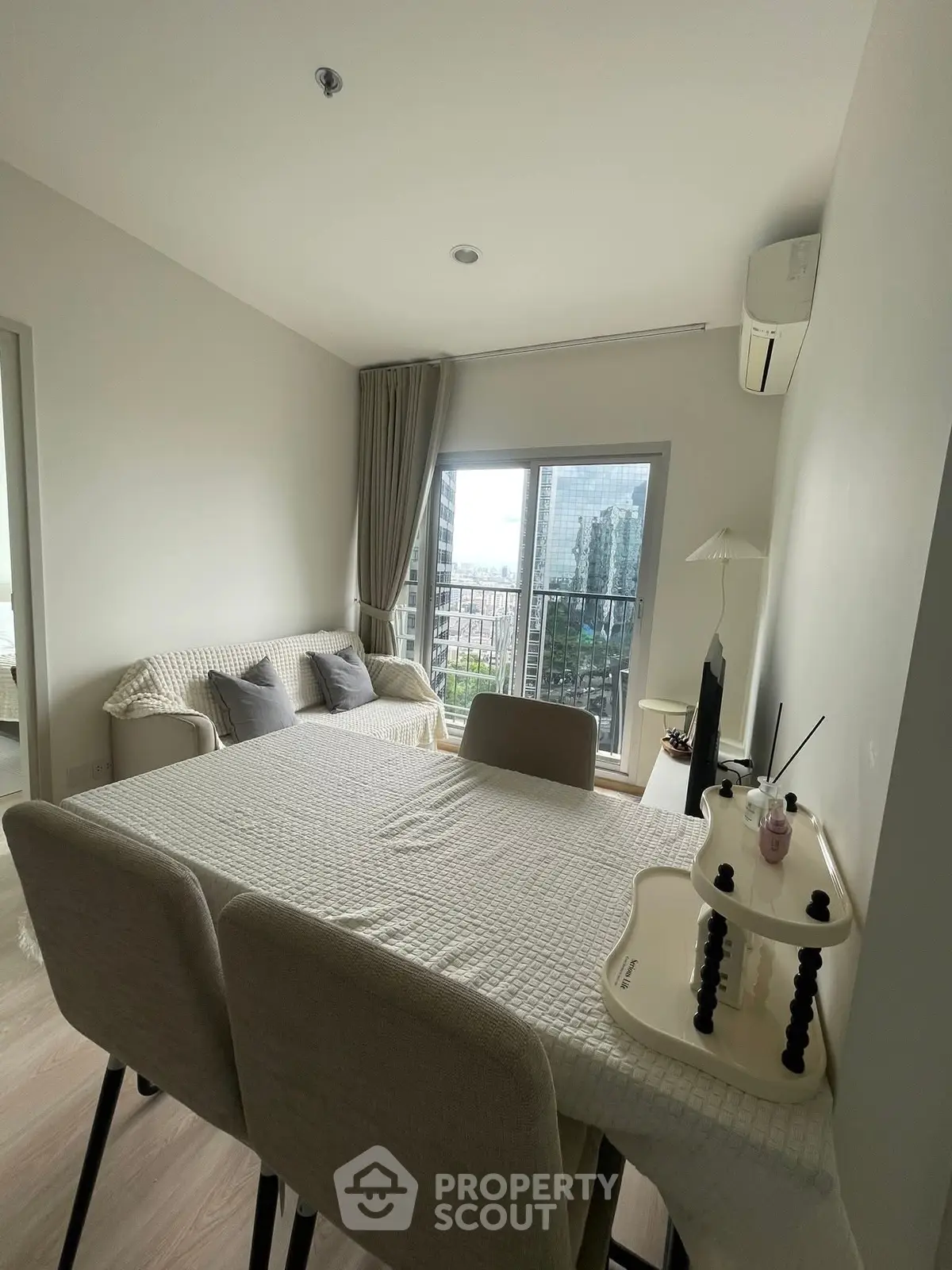 Modern living room with dining area and city view, featuring neutral decor and large windows.