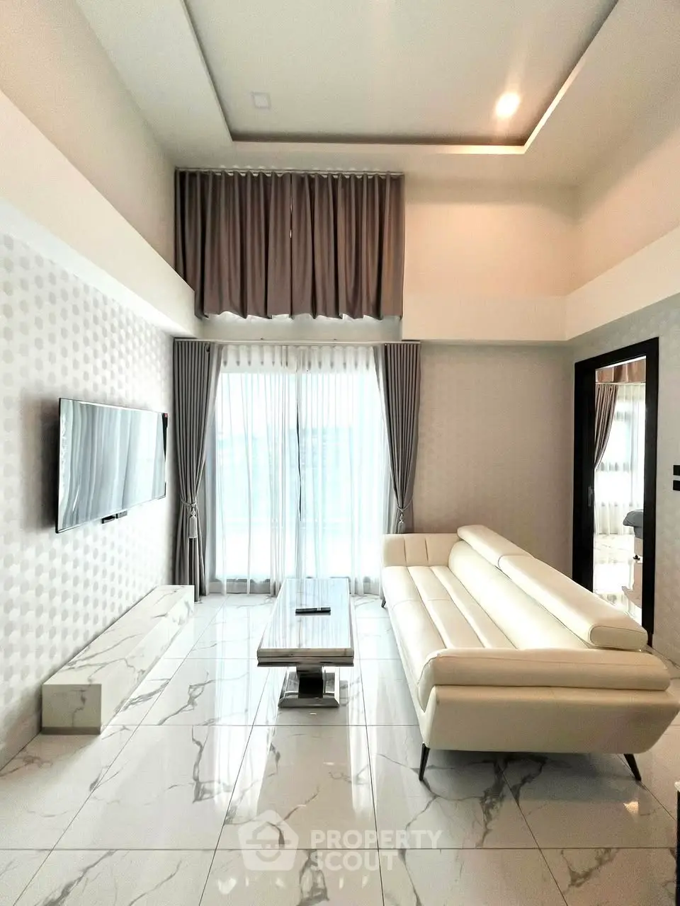 Luxurious modern living room with sleek white sofa and large TV, featuring elegant marble flooring and stylish curtains.