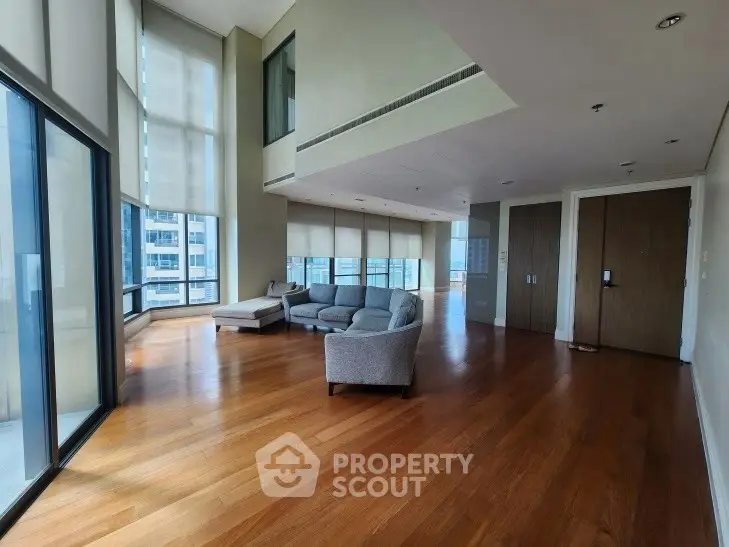 Spacious modern living room with floor-to-ceiling windows and hardwood floors in a high-rise apartment.