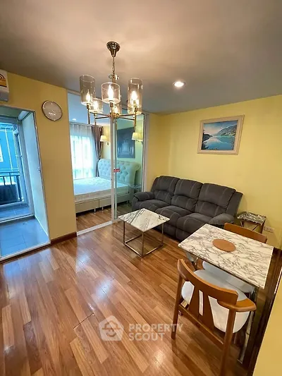 Charming living room with elegant chandelier and cozy seating, adjacent to a stylish bedroom with wooden flooring.