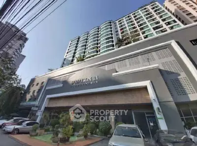 Modern condominium building exterior with lush landscaping and ample parking space.