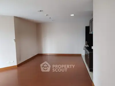 Spacious empty living room with wooden flooring and partial kitchen view.