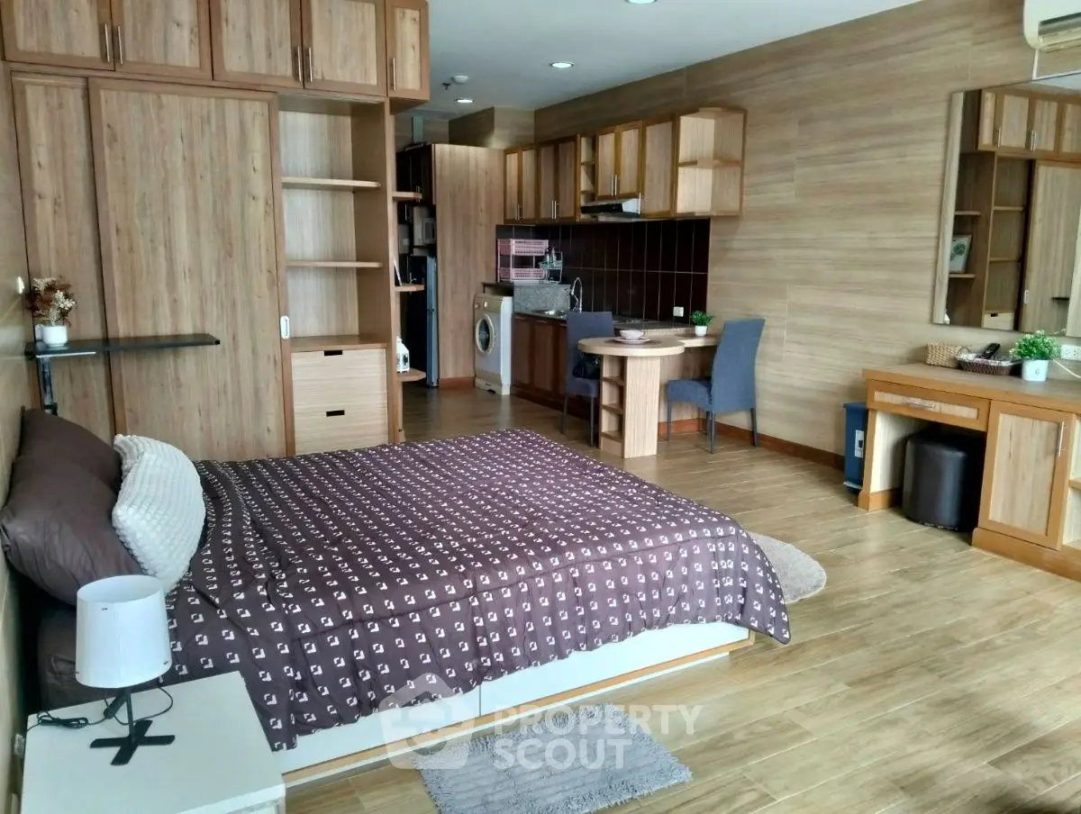 Spacious studio apartment with modern wooden furnishings and integrated kitchen area.