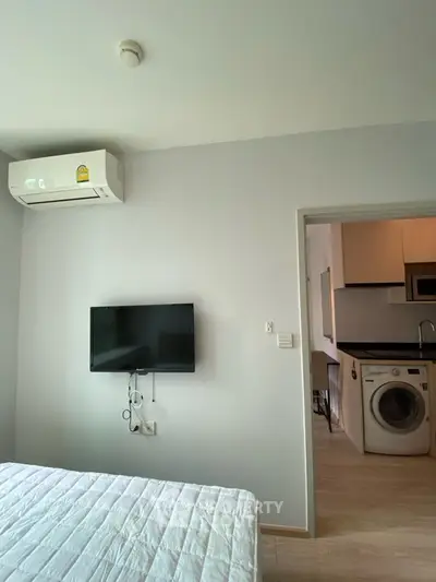 Modern bedroom with wall-mounted TV and view into kitchen with washing machine.