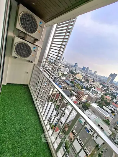 Stunning city view from a high-rise balcony with artificial grass flooring and air conditioning units.