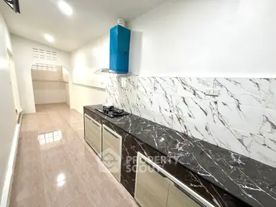 Sleek kitchen with marble countertops and modern gas stove in a bright, narrow layout.