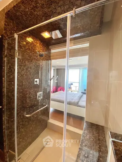Luxurious bathroom with glass shower and mosaic tiles, offering a glimpse into a cozy bedroom.