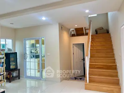 Spacious modern living area with wooden staircase and glass door leading to kitchen.