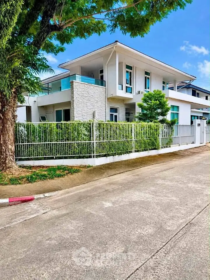 Modern two-story house with large balcony and lush greenery in a serene neighborhood.