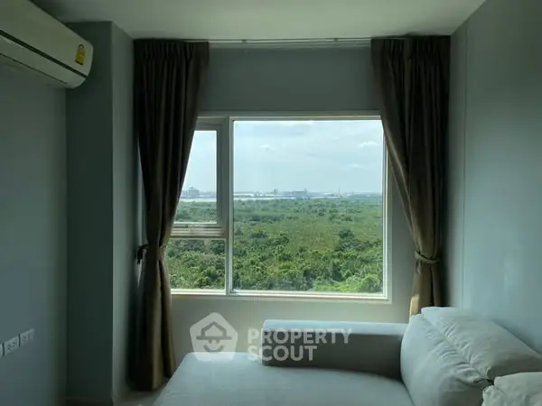 Spacious room with large window offering stunning green view and cozy seating area.