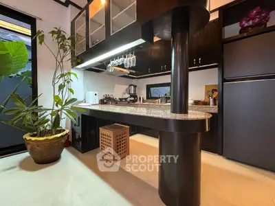Modern kitchen with sleek black cabinets and open layout, featuring a stylish breakfast bar and indoor plant decor.