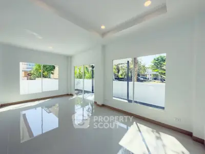 Spacious and bright living room with large windows and glossy tiled floors, offering a serene garden view.