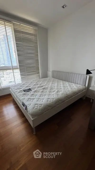 Spacious bedroom with large window and modern bed frame, featuring wooden flooring and ample natural light.