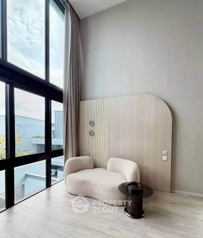 Modern living room with high ceilings and large windows, featuring stylish furniture and natural light.