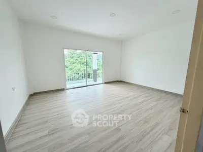 Spacious empty room with large window and balcony access, featuring light wood flooring and bright natural light.