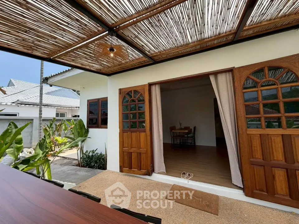 Charming bungalow with rustic wooden doors and bamboo pergola, perfect for serene outdoor living.