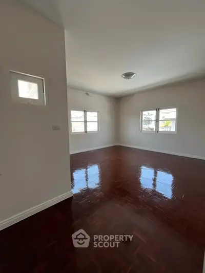 Spacious empty room with polished wooden floors and ample natural light from large windows.
