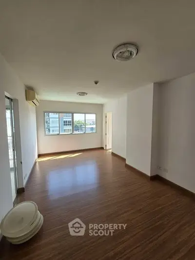 Spacious empty living room with wooden flooring and large windows offering natural light.