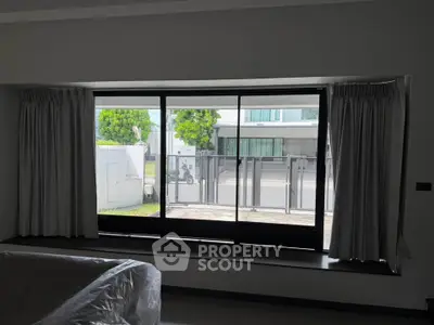 Spacious living room with large window offering a view of the modern exterior and lush greenery.
