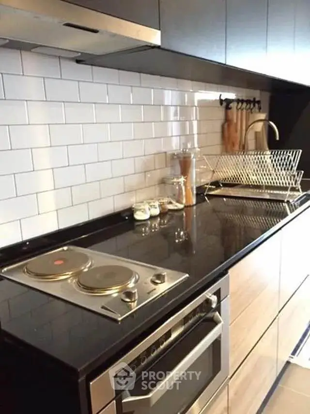 Modern kitchen with sleek black countertops and electric stove, featuring stylish subway tile backsplash.
