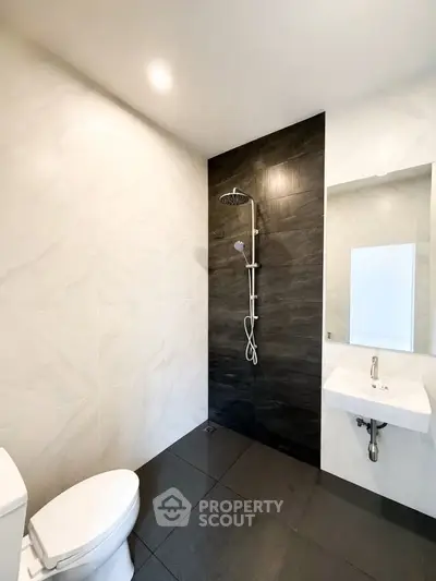 Modern bathroom with sleek black and white tiles, featuring a rain shower and minimalist fixtures.