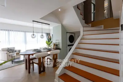 Modern open-plan living room with stylish dining area and staircase, featuring elegant decor and natural light.