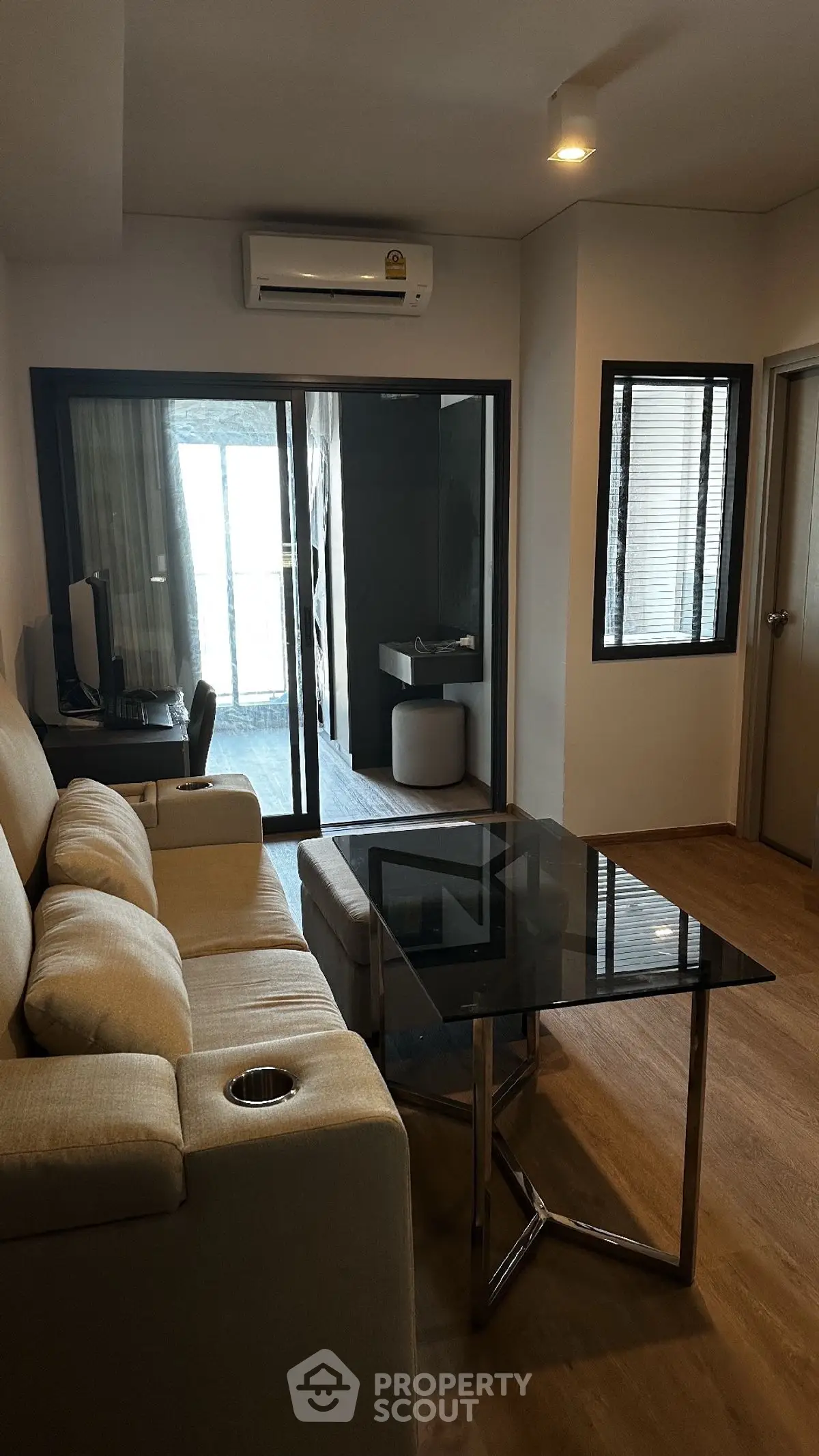 Modern living room with glass coffee table and beige sofa, featuring a study nook and air conditioning.