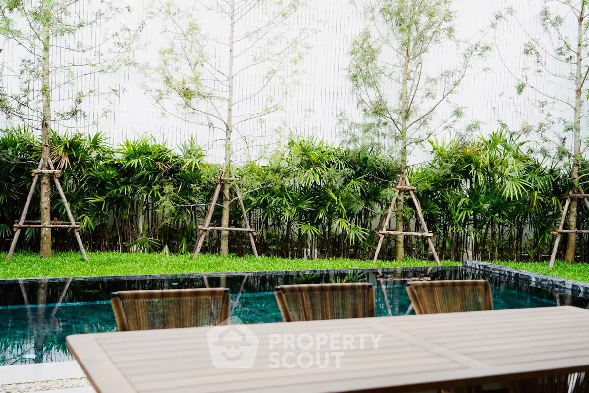 Luxurious outdoor pool area with lush greenery and elegant wooden furniture, perfect for relaxation and entertainment.