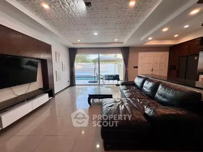 Luxurious living room with leather sofa and modern decor, featuring a large TV and open view to the pool area.