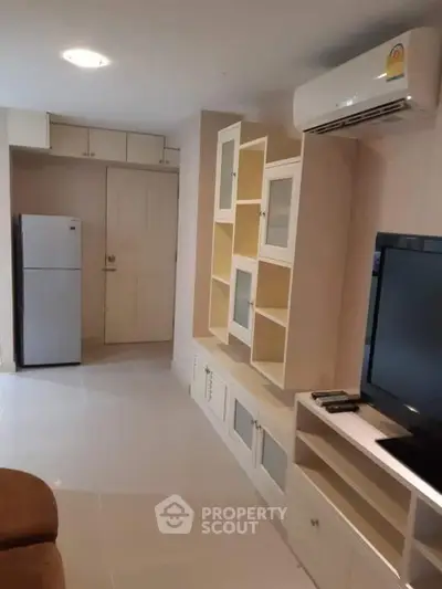 Modern living room with built-in storage and air conditioning, featuring a sleek TV setup and compact fridge.