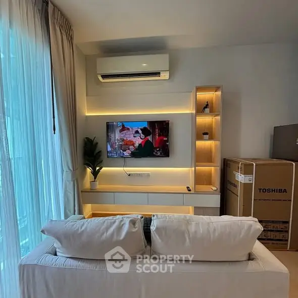 Modern living room with cozy sofa and wall-mounted TV, featuring ambient lighting and air conditioning.