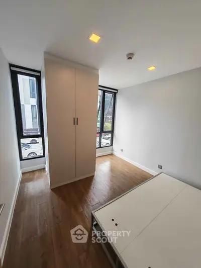 Spacious bedroom with large windows and wooden flooring in modern apartment.