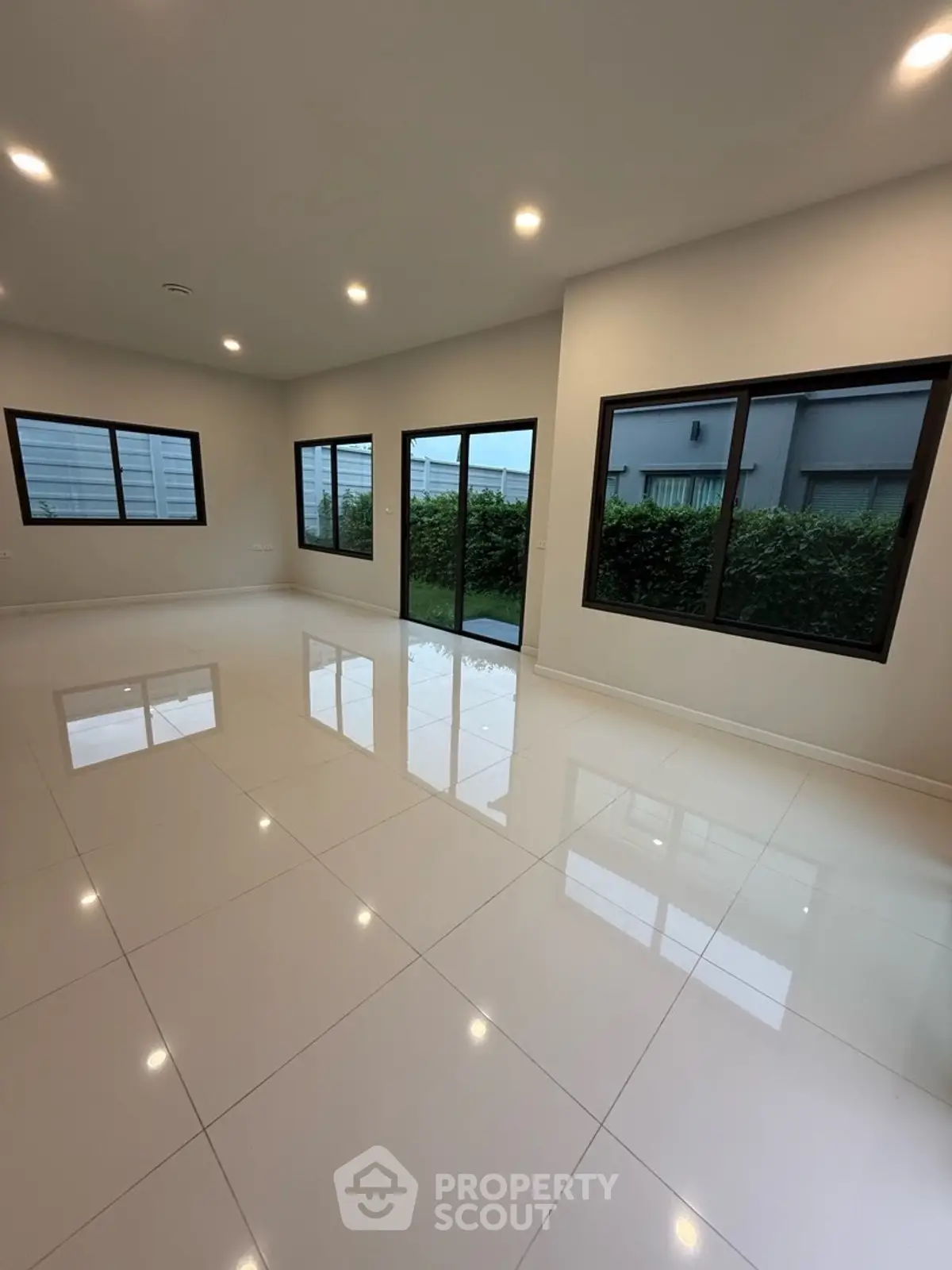 Spacious modern living room with large windows and glossy tiled floor, offering abundant natural light.