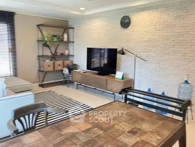 Stylish living room with modern decor, featuring a TV, wooden furniture, and a brick accent wall.
