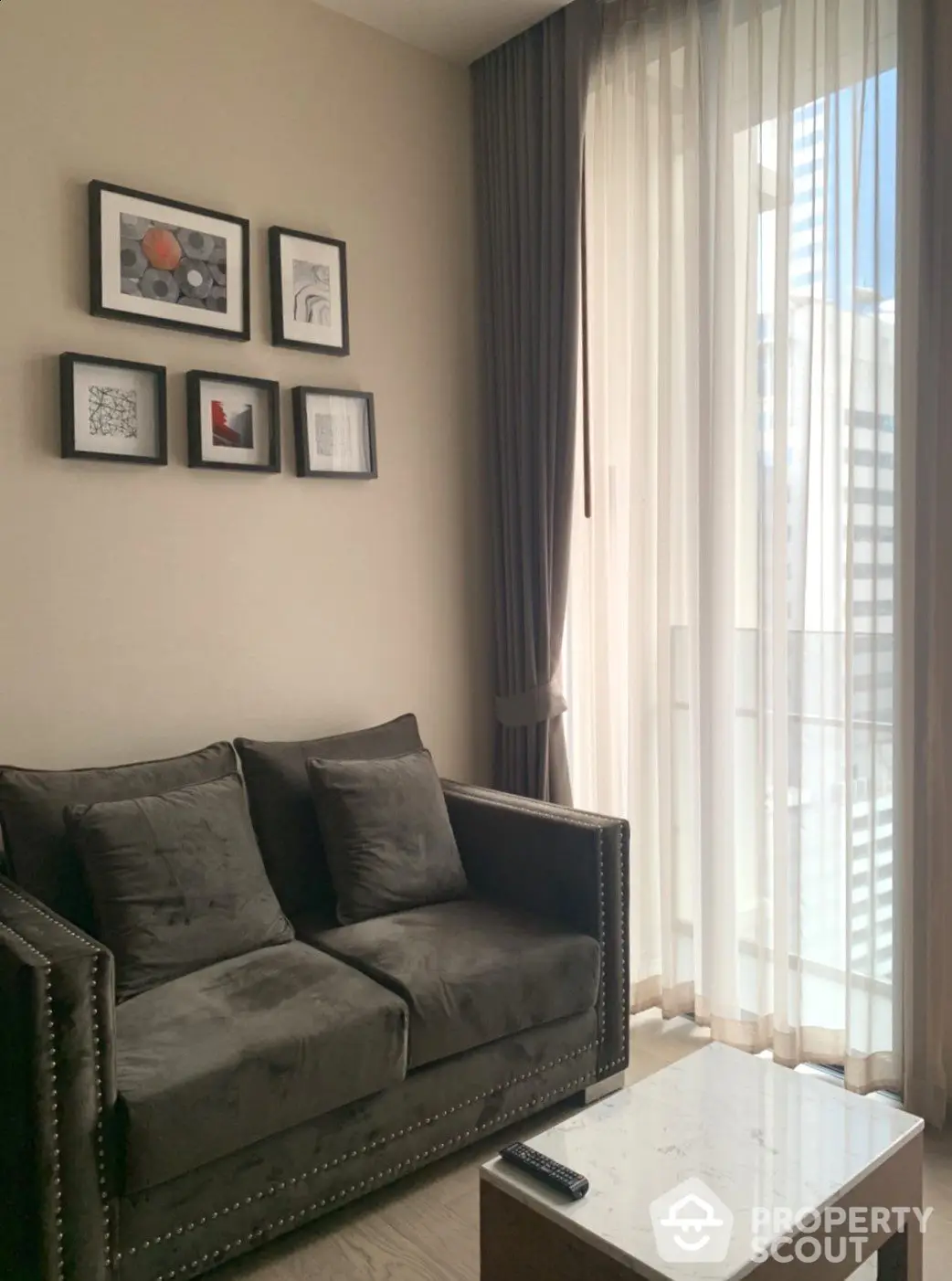 Elegant living room with plush grey sofa, marble coffee table, and chic wall art, bathed in natural light from floor-to-ceiling sheer curtains.