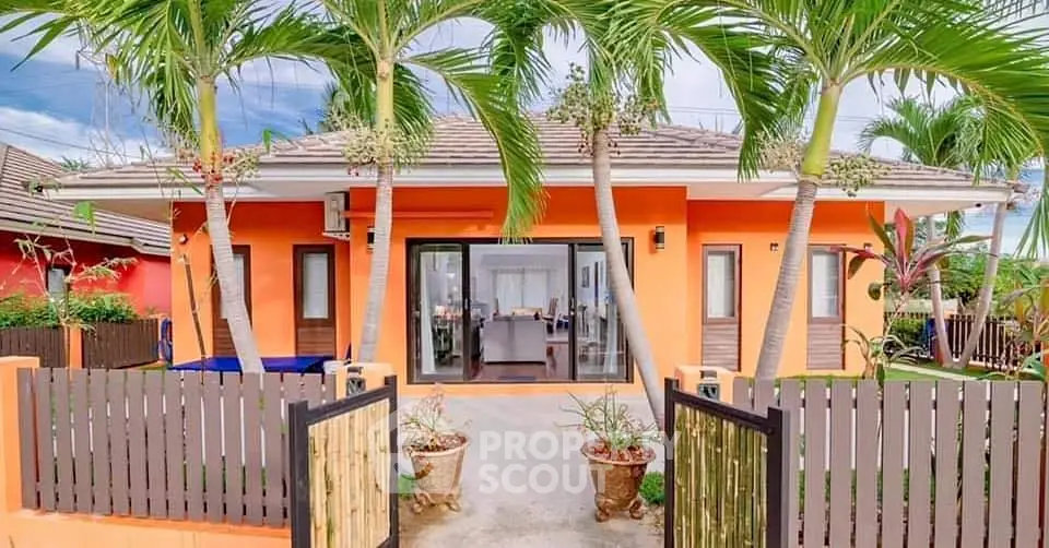 Charming tropical villa with vibrant orange facade and lush palm trees, perfect for serene living.