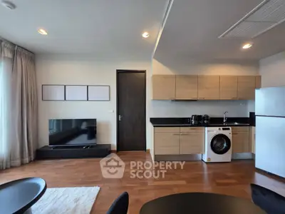 Modern open-plan living room with kitchen, featuring wooden flooring and sleek appliances.