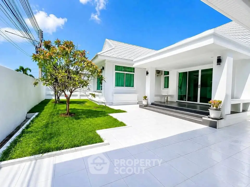 Stunning modern white house with lush green lawn and spacious patio under clear blue sky.