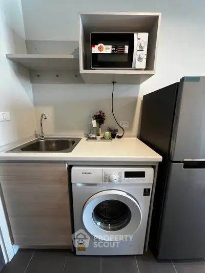Modern compact kitchen with washing machine, microwave, and fridge in sleek design.