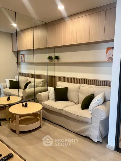 Modern living room with stylish beige sofa, mirrored wall, and wooden shelves for a cozy ambiance.