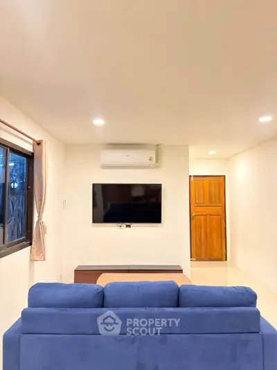 Modern living room with blue sofa, wall-mounted TV, and air conditioning unit.