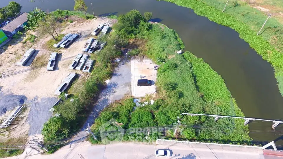 Aerial view of a riverside plot with potential for development, surrounded by greenery and accessible by road.