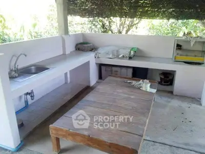 Outdoor kitchen with rustic wooden table and tiled countertops in a serene garden setting.