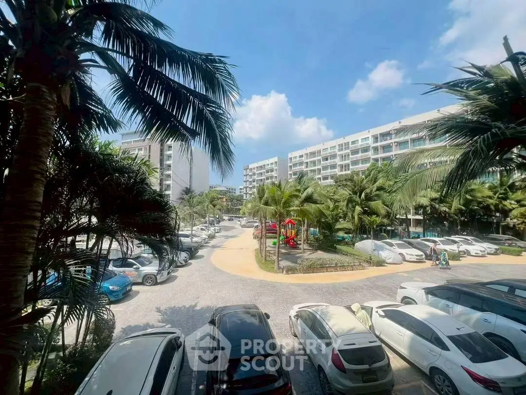 Spacious parking area with lush palm trees and modern apartment buildings under a clear blue sky.