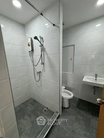 Modern bathroom with sleek shower and white tiles, featuring a compact design and contemporary fixtures.