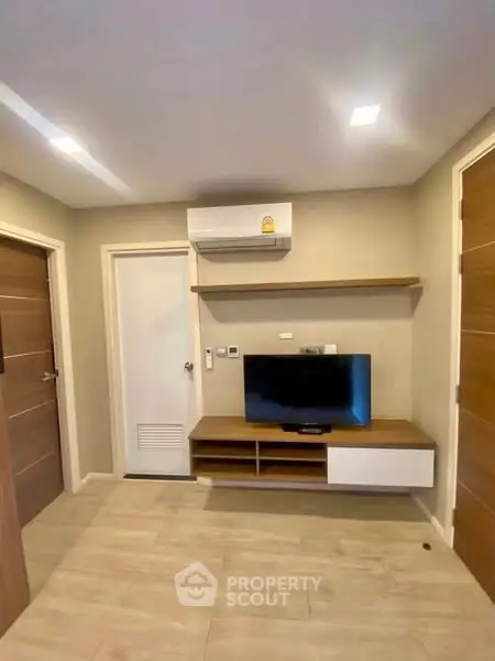 Modern living room with TV and air conditioning unit, featuring sleek wooden flooring.