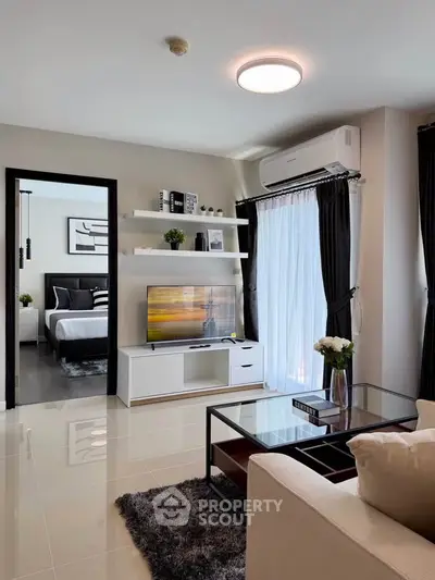 Modern living room with sleek design, featuring a cozy sofa, glass coffee table, and a view into a stylish bedroom.