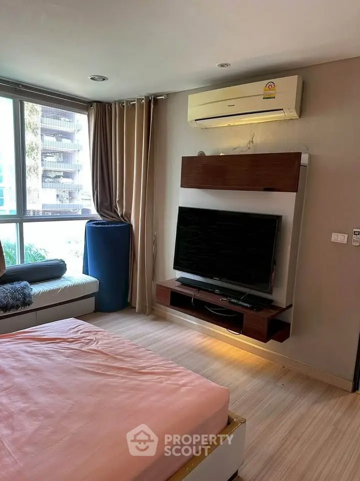 Modern bedroom with large window, wall-mounted TV, and air conditioning unit, offering comfort and style.